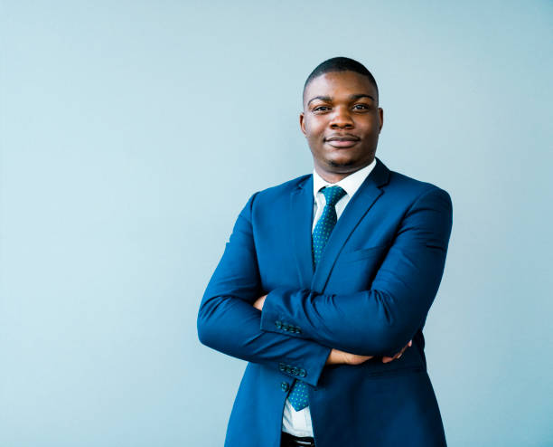 Portrait of confident businessman with arms crossed. Male entrepreneur is wearing blue suit. He is standing against gray background.